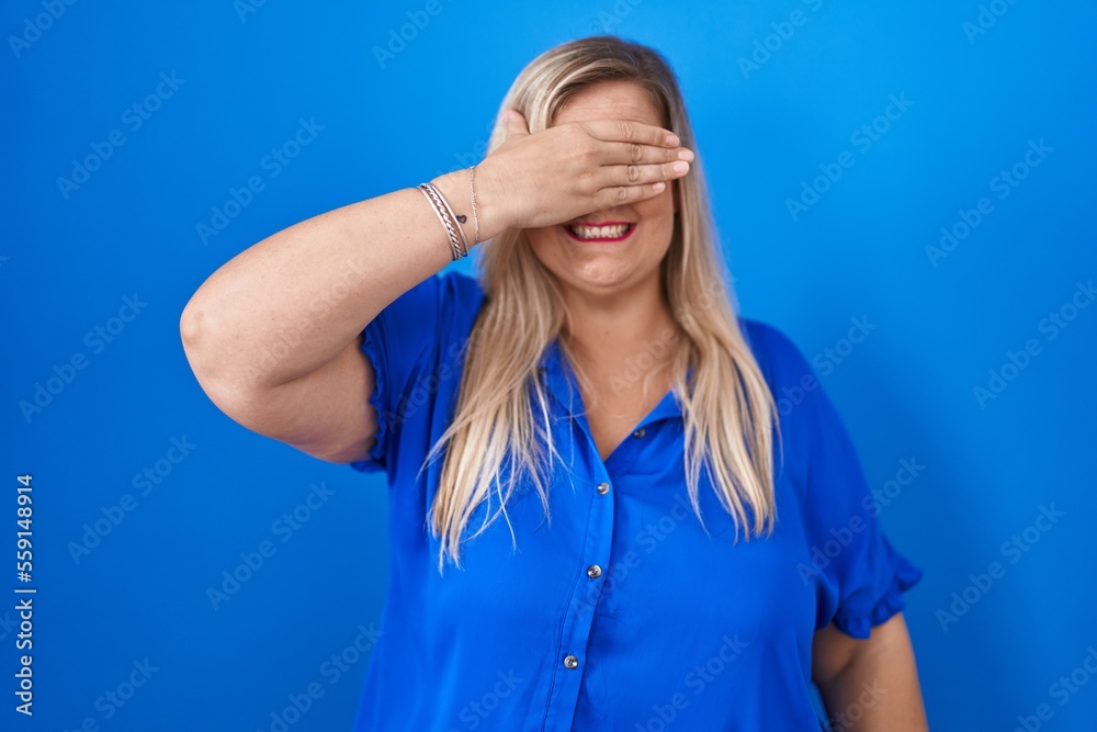 Caucasian plus size woman standing over blue background smiling and laughing with hand on face covering eyes for surprise. blind concept. Caucasian plus size woman standing over blue background smiling and laughing with hand on face covering eyes for surprise. blind concept.