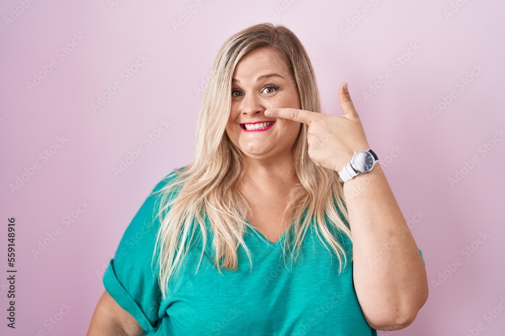 Caucasian plus size woman standing over pink background pointing with hand finger to face and nose, smiling cheerful. beauty concept Caucasian plus size woman standing over pink background pointing with hand finger to face and nose, smiling cheerful. beauty concept