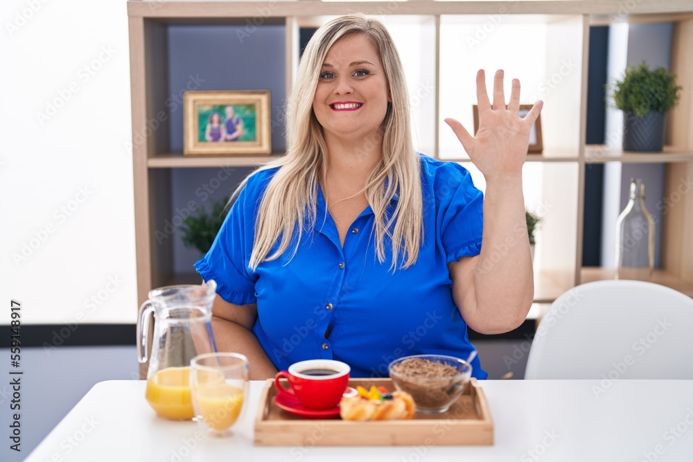 Caucasian plus size woman eating breakfast at home showing and pointing up with fingers number five while smiling confident and happy. Caucasian plus size woman eating breakfast at home showing and pointing up with fingers number five while smiling confident and happy.