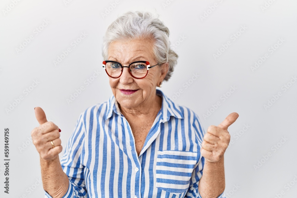 Senior woman with grey hair standing over white background success sign doing positive gesture with hand, thumbs up smiling and happy. cheerful expression and winner gesture. Senior woman with grey hair standing over white background success sign doing positive gesture with hand, thumbs up smiling and happy. cheerful expression and winner gesture.