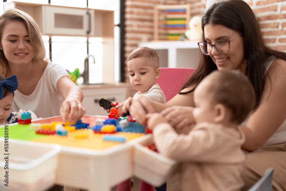Teachers and preschool students playing with construction blocks sitting on table at kindergarten Teachers and preschool students playing with construction blocks sitting on table at kindergarten