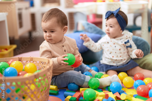 Two toddlers playing with balls sitting on floor at kindergarten