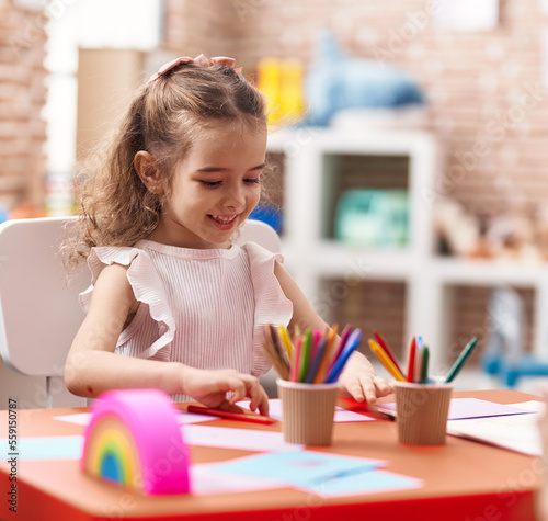 Adorable caucasian girl sitting on table drawing on paper at classroom