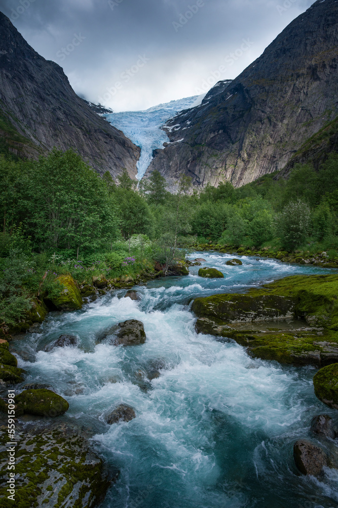 Mountain river with ice cold water of Briksdalsbreen glacier in the mountains of Jostedalsbreen national park in Norway, moody atmosphere, rocks in the water Mountain river with ice cold water of Briksdalsbreen glacier in the mountains of Jostedalsbreen national park in Norway, moody atmosphere, rocks in the water