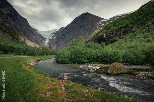 Fototapeta Naklejka Na Ścianę i Meble -  Mountain river with ice cold water of Briksdalsbreen glacier in the mountains of Jostedalsbreen national park in Norway, moody atmosphere, rocks in the water