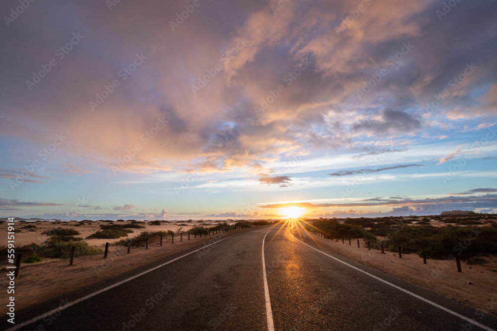 Sunrise over the sand dunes and a dune road. Light drifts from cars, Corralejo National Park in the morning, Las Palmas Province, Fuerteventura, Canary Islands, Spain Sunrise over the sand dunes and a dune road. Light drifts from cars, Corralejo National Park in the morning, Las Palmas Province, Fuerteventura, Canary Islands, Spain