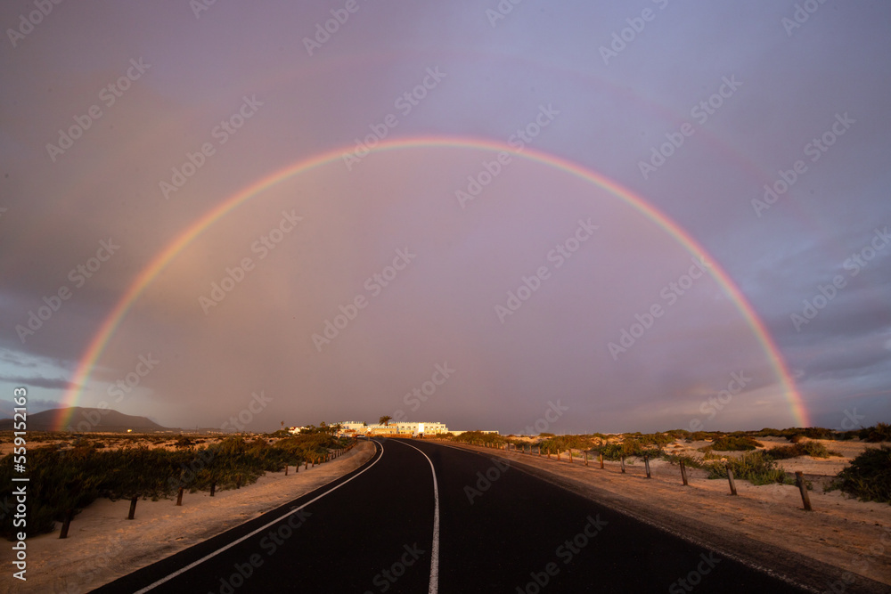 Rainbow over sand dunes and a dune road. Corralejo National Park in the morning, Las Palmas Province, Fuerteventura, Canary Islands, Spain