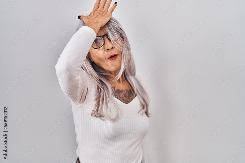 Middle age woman with grey hair standing over white background surprised with hand on head for mistake, remember error. forgot, bad memory concept. Middle age woman with grey hair standing over white background surprised with hand on head for mistake, remember error. forgot, bad memory concept.