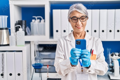 Middle age grey-haired woman scientist using smartphone working at laboratory