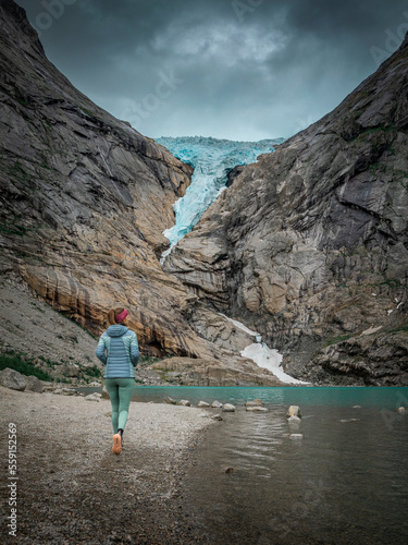 Woman hiking along beach of glacier lake at Briksdalsbreen glacier in the mountains of Jostedalsbreen national park in Norway, turquoise water and blue ice