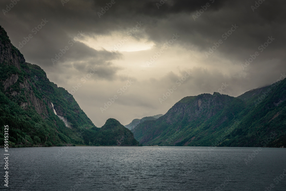 Norwegian fjord with waterfall in the mountains and dark moody clouds in the sky