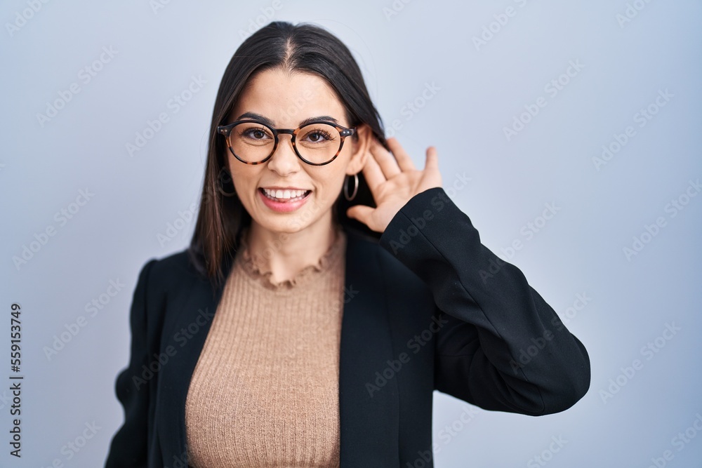 Young brunette woman standing over blue background smiling with hand over ear listening an hearing to rumor or gossip. deafness concept. Young brunette woman standing over blue background smiling with hand over ear listening an hearing to rumor or gossip. deafness concept.