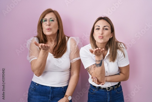 Hispanic mother and daughter wearing casual white t shirt over pink background looking at the camera blowing a kiss with hand on air being lovely and sexy. love expression. © Krakenimages.com