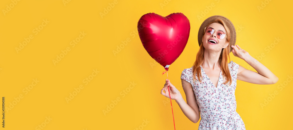cheerful girl in straw hat and sunglasses hold love heart balloon on yellow background. Woman isolated face portrait, banner with copy space. cheerful girl in straw hat and sunglasses hold love heart balloon on yellow background. Woman isolated face portrait, banner with copy space.