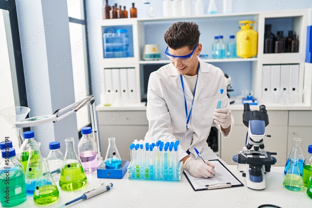 Young hispanic man wearing scientist uniform writing on clipboard at laboratory Young hispanic man wearing scientist uniform writing on clipboard at laboratory