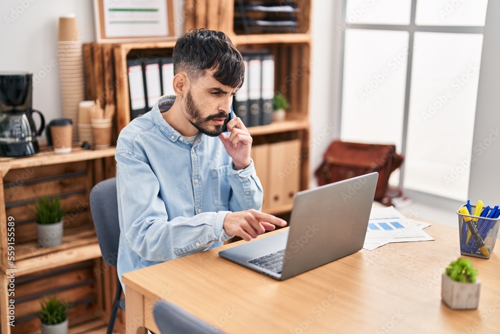 Young hispanic man business worker talking on smartphone using laptop at office Young hispanic man business worker talking on smartphone using laptop at office