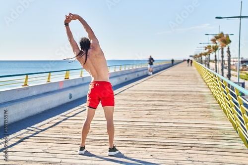 Young man stretching arms on back view at seaside