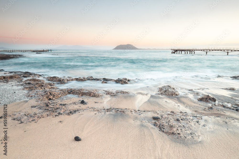 Beautiful morning on the sandy beach. Long exposure at the sea. Milky sunrise in haze and fog. Corralejo, Canary Islands, Spain