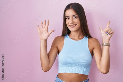 Young brunette woman standing over pink background showing and pointing up with fingers number seven while smiling confident and happy.