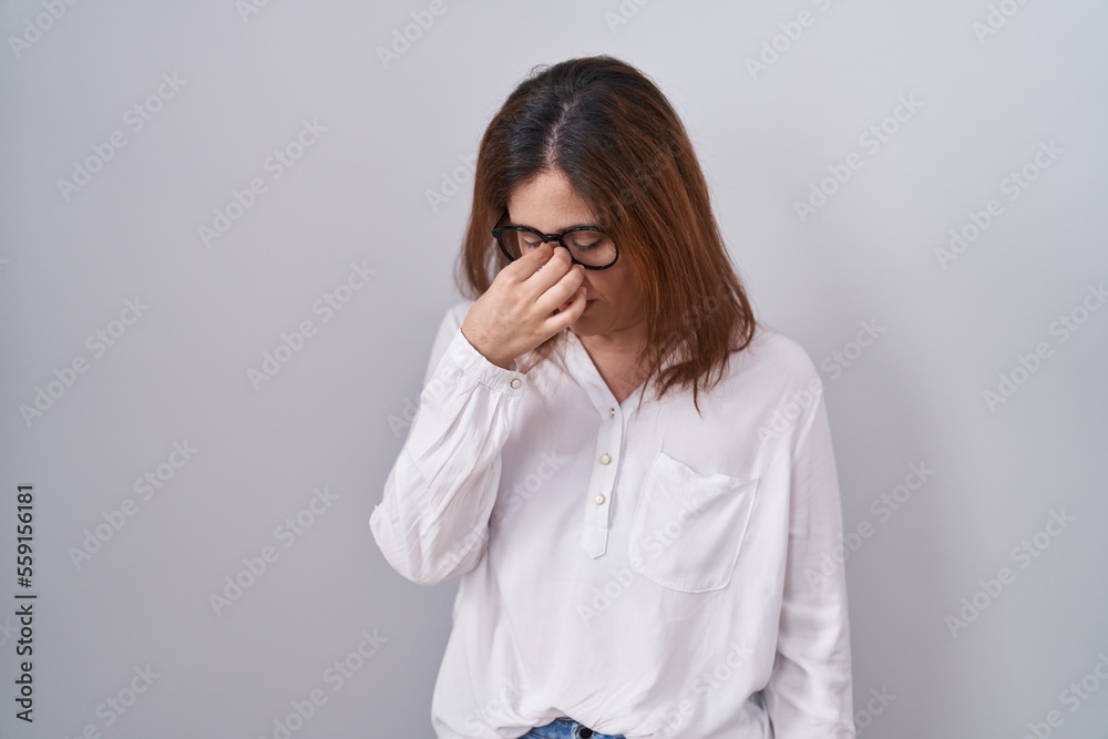 Brunette woman standing over white isolated background tired rubbing nose and eyes feeling fatigue and headache. stress and frustration concept.