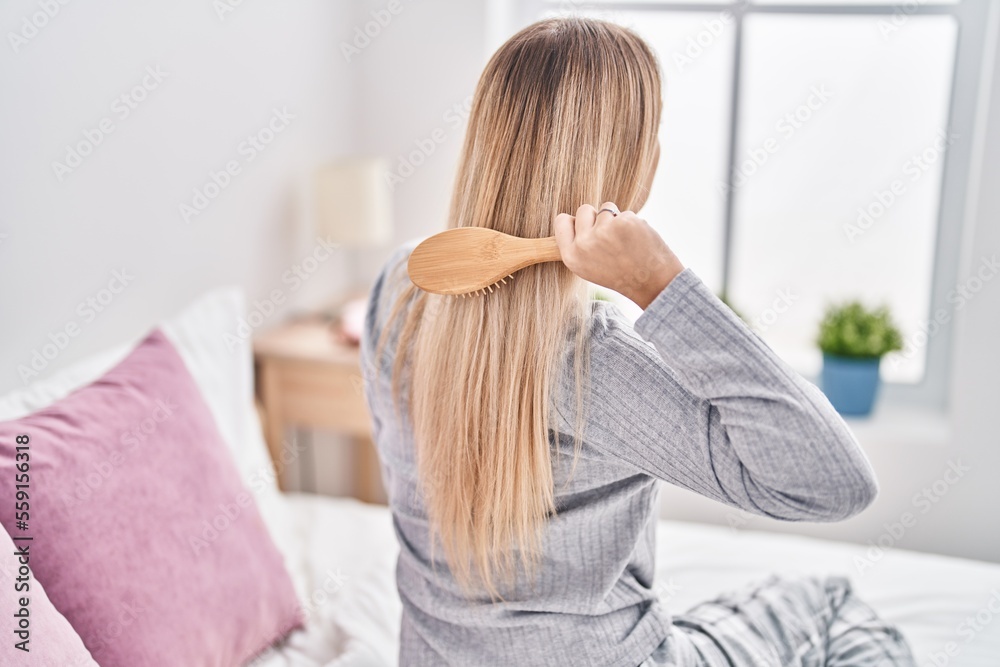 Young woman combing hair sitting on bed at bedroom Young woman combing hair sitting on bed at bedroom