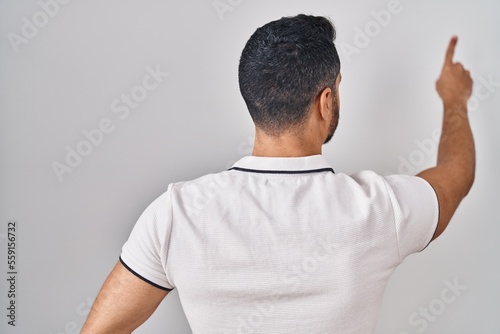 Young hispanic man with beard wearing casual clothes over white background posing backwards pointing ahead with finger hand
