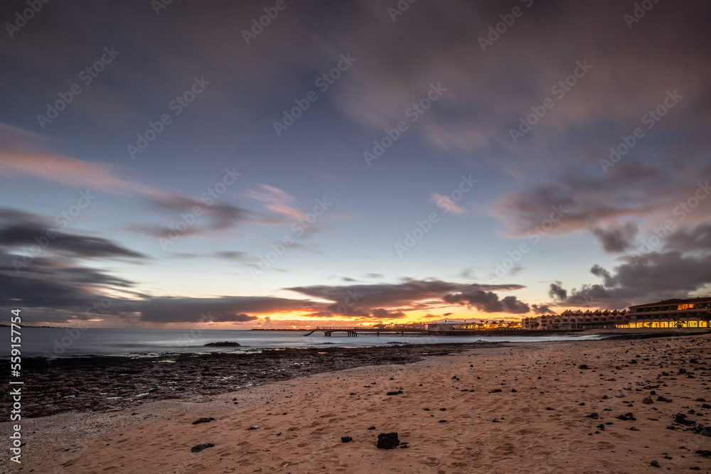 Sunrise on the beach, lava rock and sandy beach in a long exposure. Romantic place with pier in the morning. Playa de la Barreta, Corralejo National Park, Canary Islands, Spain