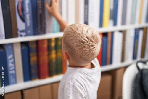 Adorable toddler holding book of shelving at classroom