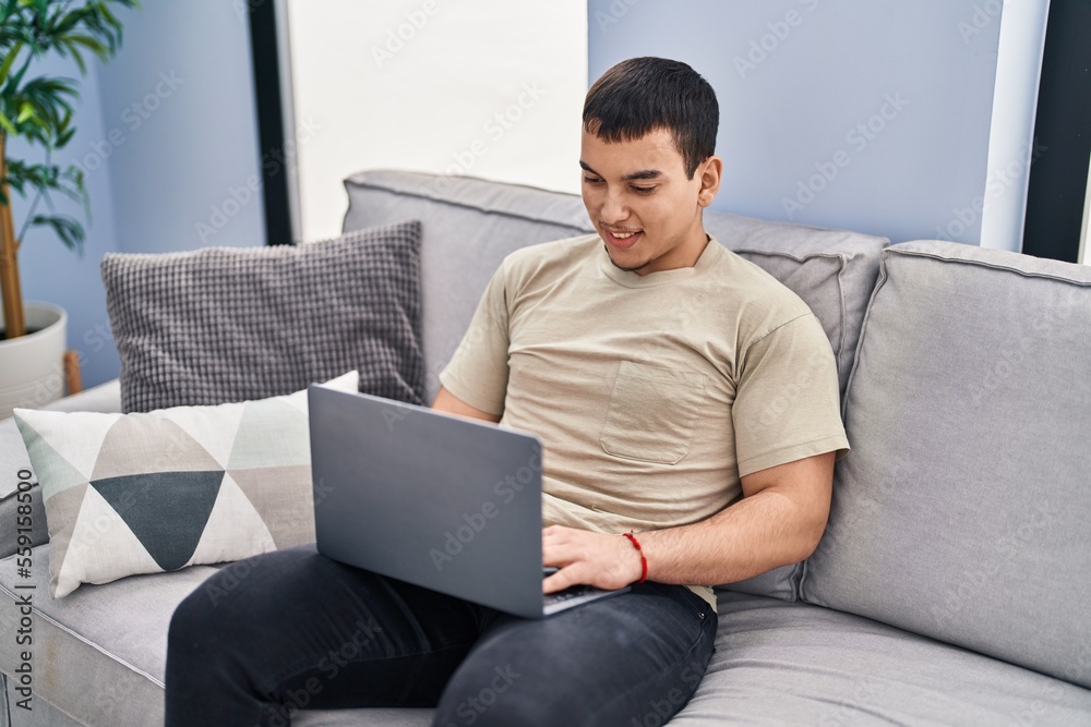 Young man using laptop sitting on sofa at home Young man using laptop sitting on sofa at home