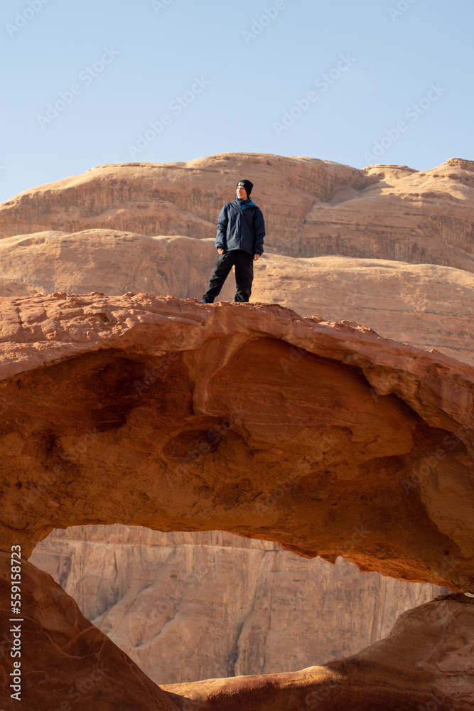 boy standing on arch in the desert