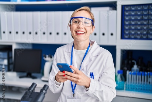 Leinwand Poster Young blonde woman scientist smiling confident using smartphone at laboratory