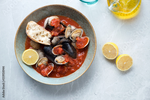 Plate of tomato broth with mussels and vongole on a light-grey granite background, horizontal shot, view from above