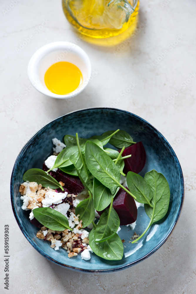 Fresh spinach, beetroot and goat cheese salad served in a dark-blue bowl, vertical shot on a beige stone background