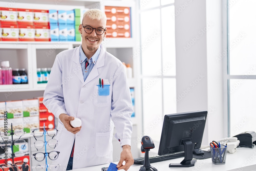Fototapeta premium Young caucasian man pharmacist holding pills bottle using data phone and credit card at pharmacy