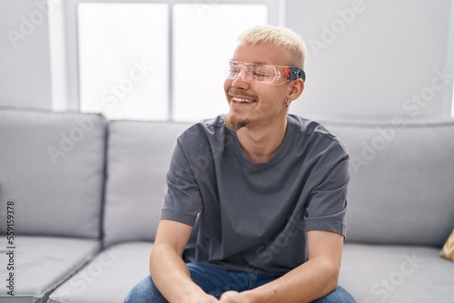 Young caucasian man wearing virtual reality glasses looking away to side with smile on face, natural expression. laughing confident.