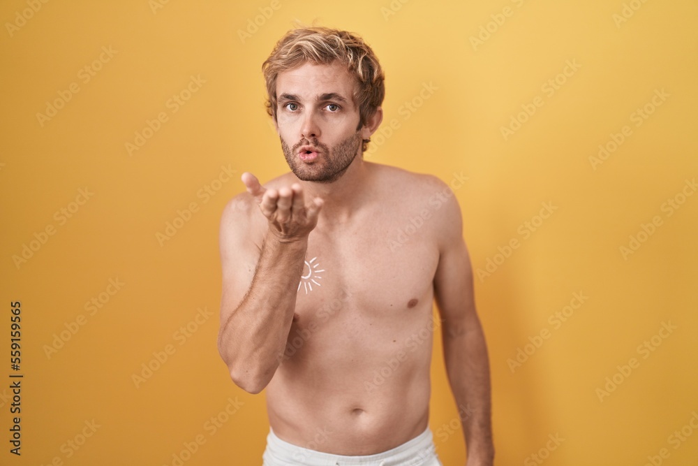 Fototapeta premium Caucasian man standing shirtless wearing sun screen looking at the camera blowing a kiss with hand on air being lovely and sexy. love expression.