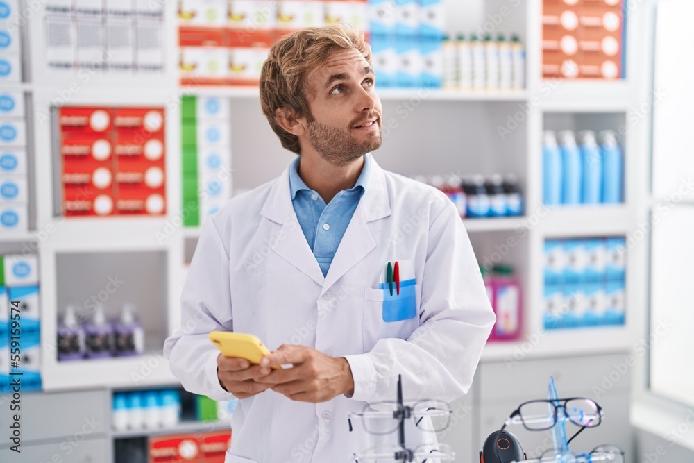 Young man pharmacist using smartphone working at pharmacy