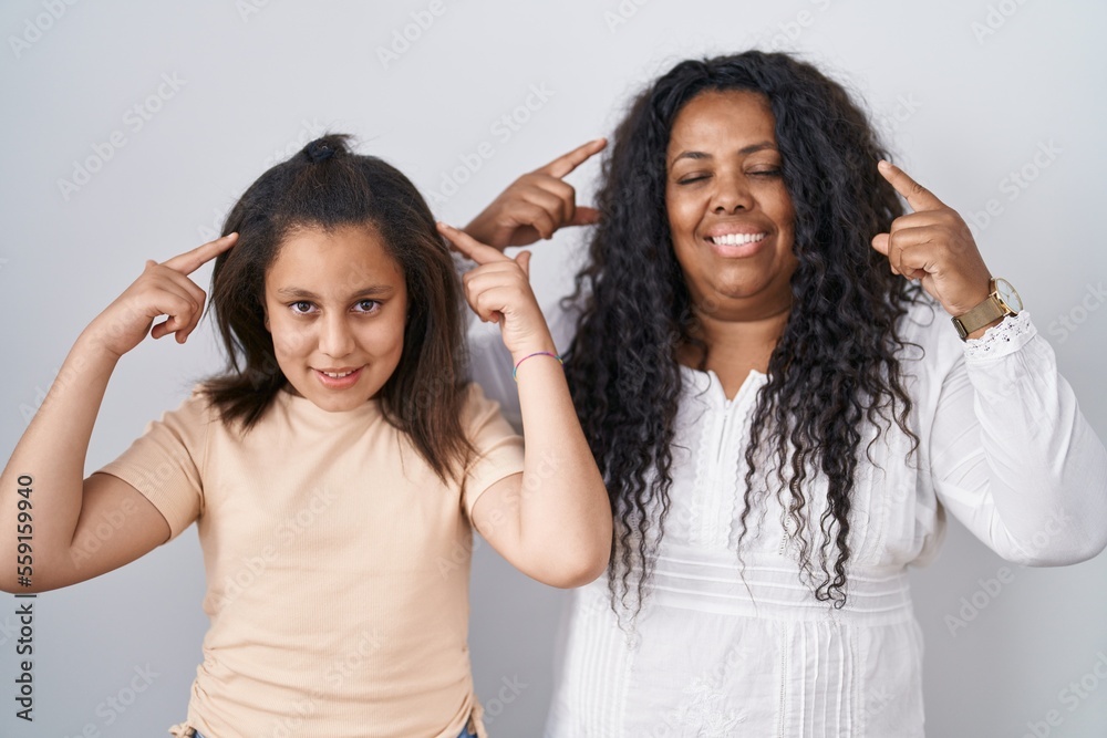 Mother and young daughter standing over white background smiling pointing to head with both hands finger, great idea or thought, good memory Mother and young daughter standing over white background smiling pointing to head with both hands finger, great idea or thought, good memory