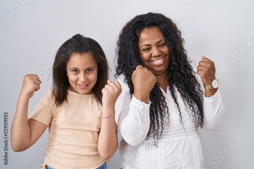 Mother and young daughter standing over white background very happy and excited doing winner gesture with arms raised  smiling and screaming for success. celebration concept.