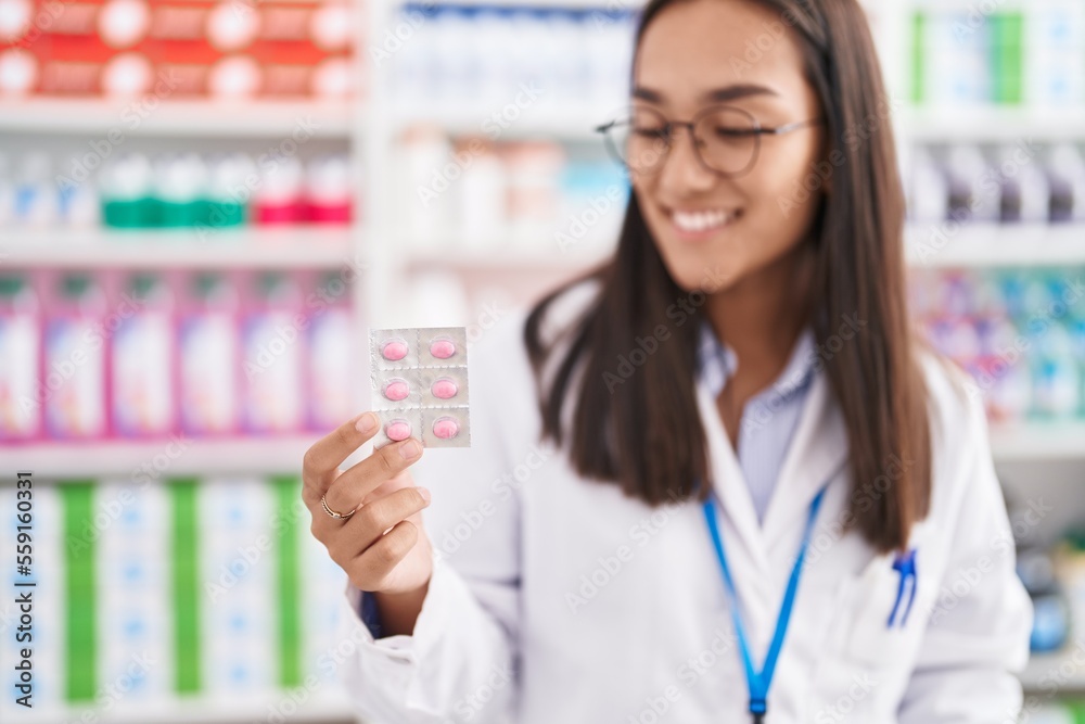 Young beautiful hispanic woman pharmacist smiling confident holding pills tablet at pharmacy