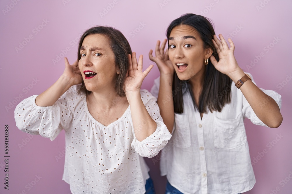 Hispanic mother and daughter together trying to hear both hands on ear gesture, curious for gossip. hearing problem, deaf Hispanic mother and daughter together trying to hear both hands on ear gesture, curious for gossip. hearing problem, deaf