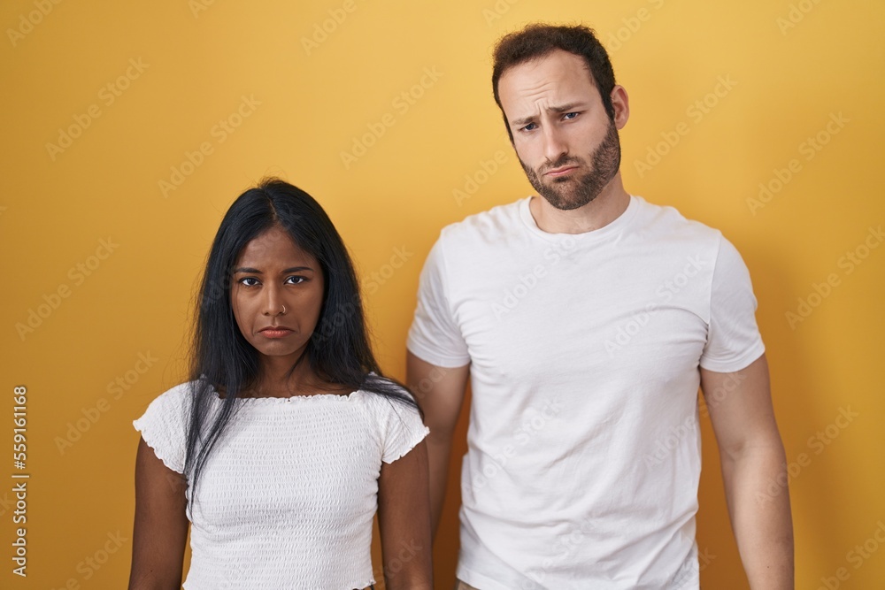 Interracial couple standing over yellow background depressed and worry for distress, crying angry and afraid. sad expression. Interracial couple standing over yellow background depressed and worry for distress, crying angry and afraid. sad expression.