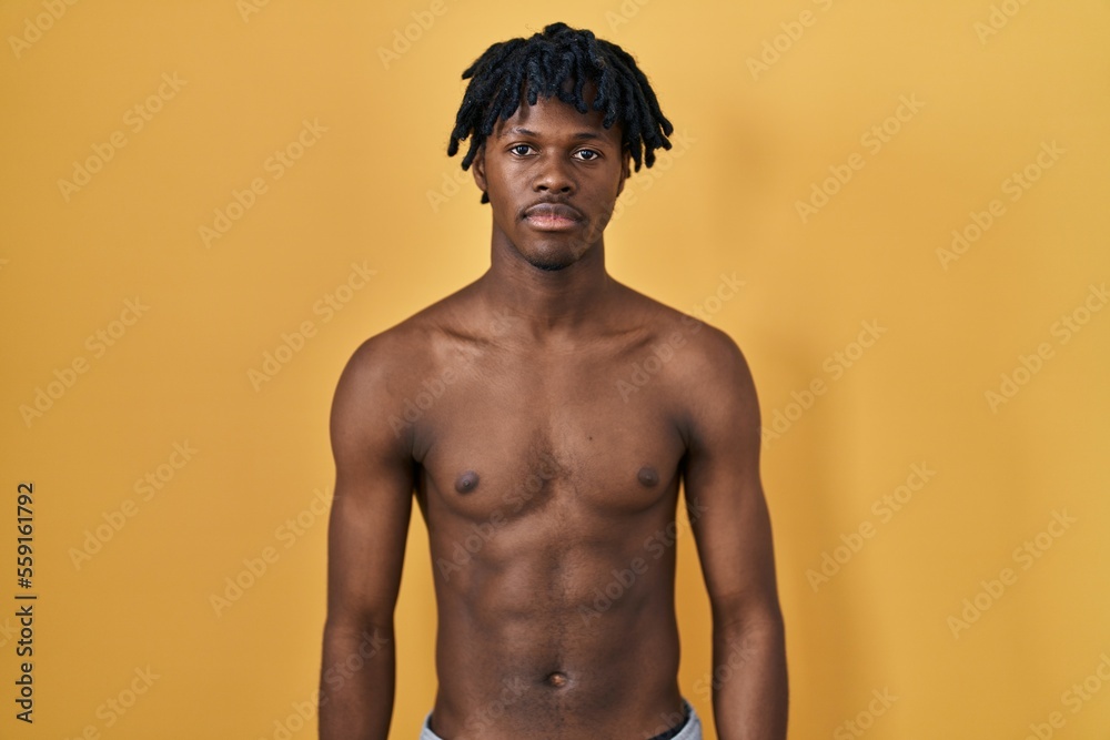 Fototapeta premium Young african man with dreadlocks standing shirtless relaxed with serious expression on face. simple and natural looking at the camera.