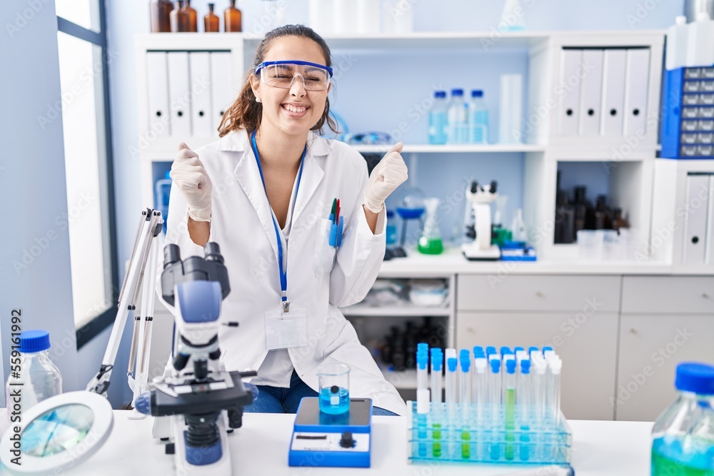 Young hispanic woman working at scientist laboratory excited for success with arms raised and eyes closed celebrating victory smiling. winner concept. Young hispanic woman working at scientist laboratory excited for success with arms raised and eyes closed celebrating victory smiling. winner concept.