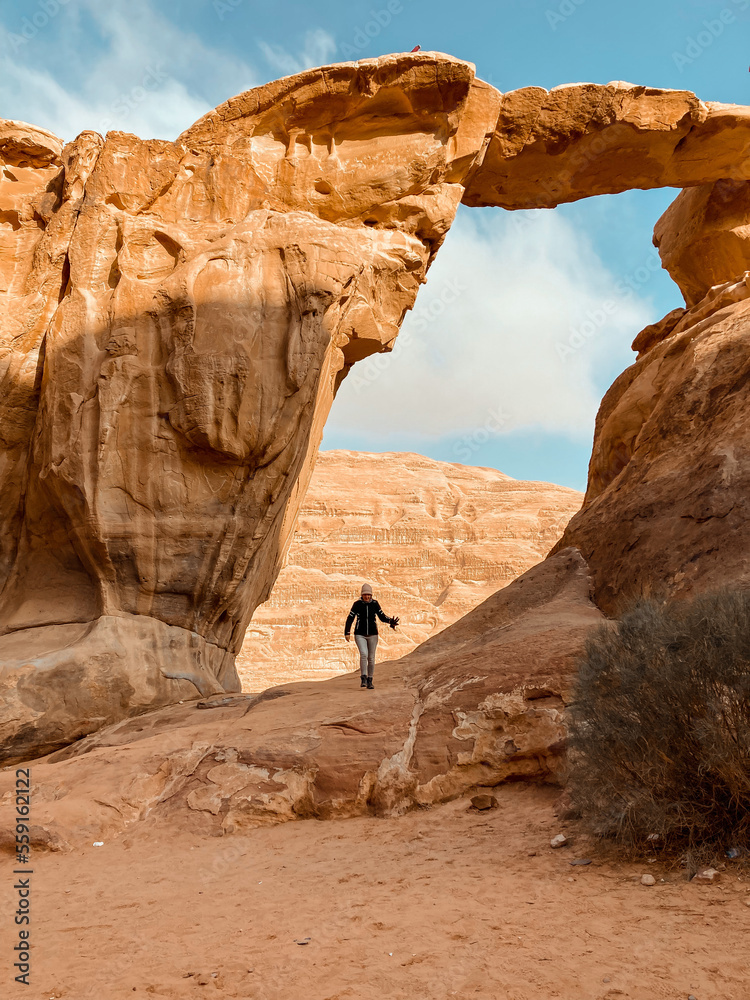 person in the desert, under an arch in wadi rum, jordan