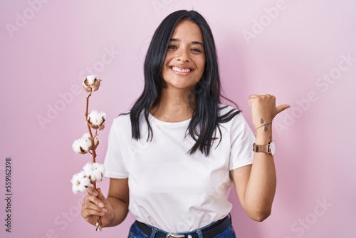 Brunette woman standing over pink background pointing to the back behind with hand and thumbs up, smiling confident