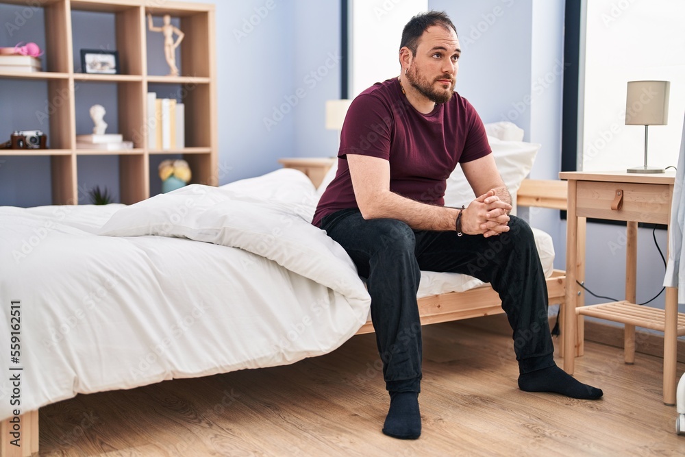 Young hispanic man sitting on bed with sad expression at bedroom