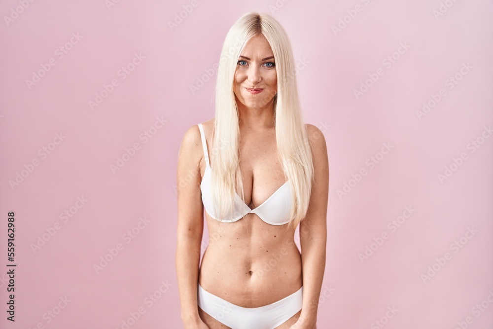 Caucasian woman wearing lingerie over pink background puffing cheeks with funny face. mouth inflated with air, crazy expression.
