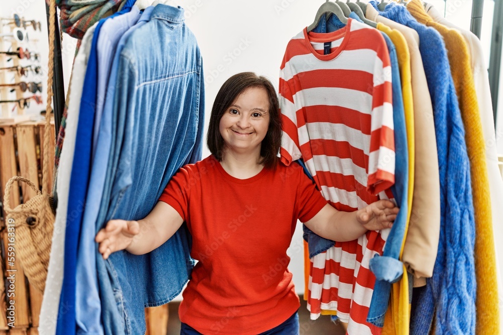 Fototapeta premium Brunette woman with down syndrome standing between hangers with different clothes at retail shop