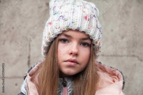 Winter portrait fashionable teen girl in winter fashion clothes, hat posing and looking at camera at grey wall background. Positive teenage emotion outdoors. Copy text space for advertisement © Alex Vog